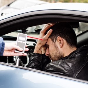 Police officer conducting a breathalyzer test on a distressed driver inside a vehicle - Law Firm of Aaron Bortel